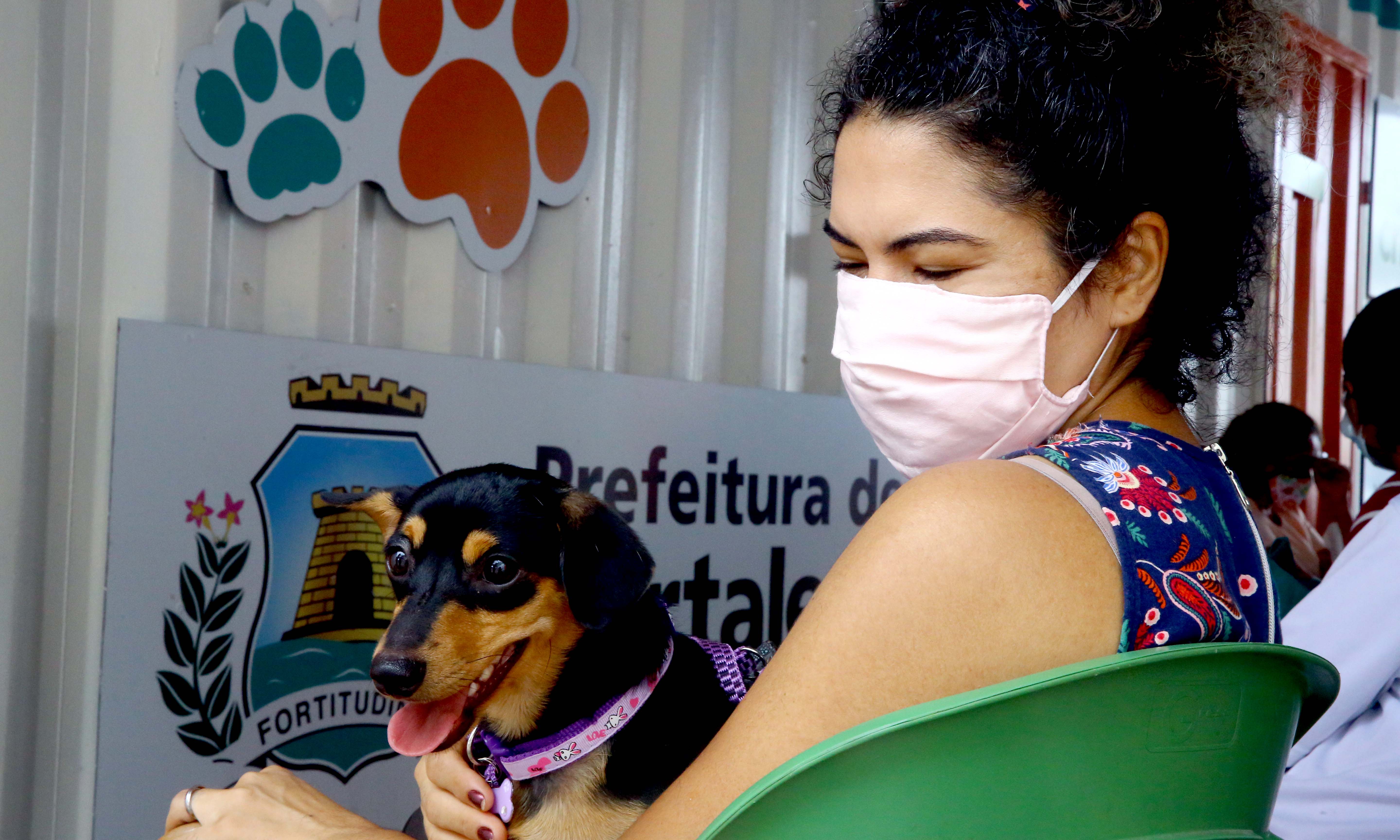 uma mulher com máscara segura um cachorro no colo